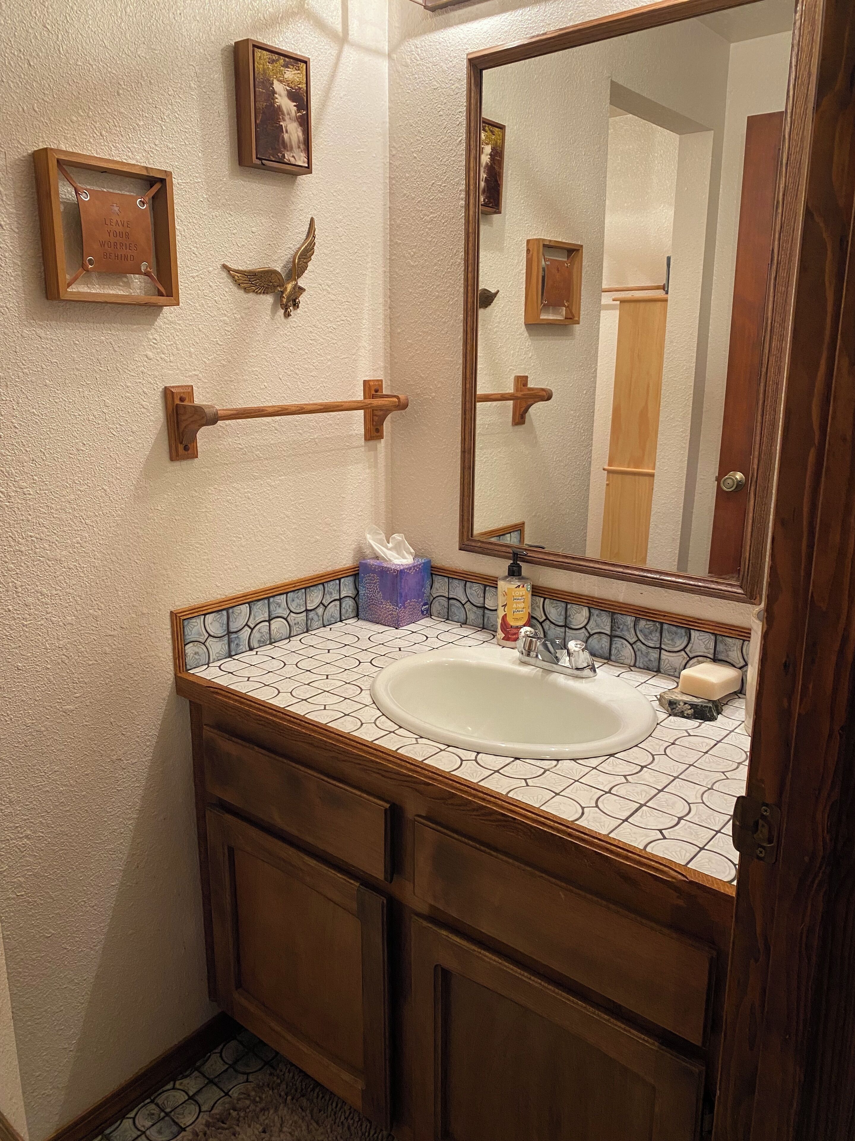 Une salle de bain avec un meuble-lavabo en bois, un grand miroir et un pare-feu en carreaux.