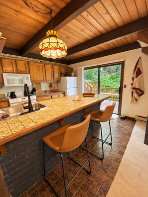 Una cocina con una isla grande, taburetes de bar, armarios de madera y una lámpara colgante.