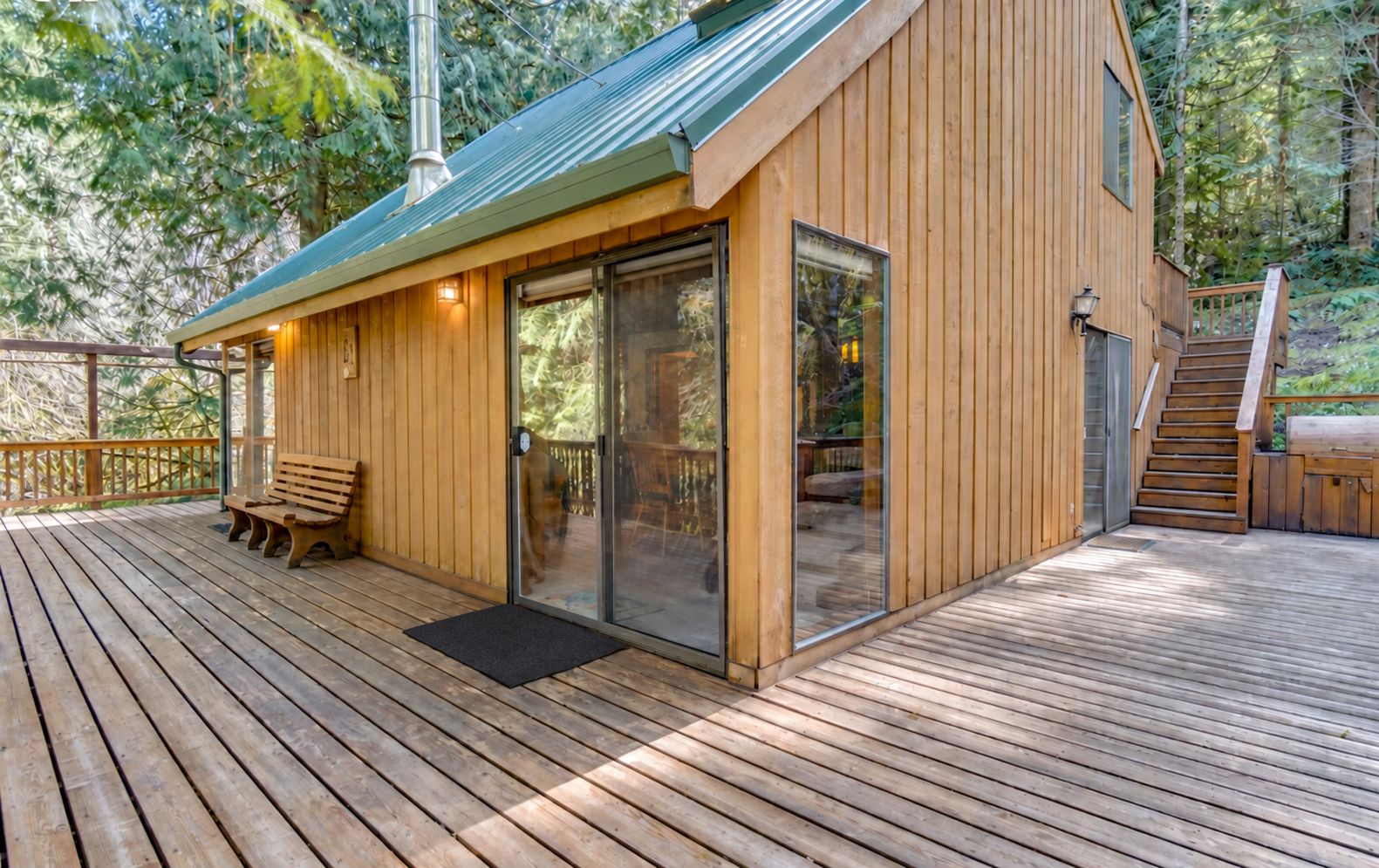 A wooden deck with a bench, a glass door entrance, and a staircase leading to an upper level.