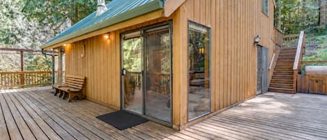 A wooden deck with a bench, a glass door entrance, and a staircase leading to an upper level.