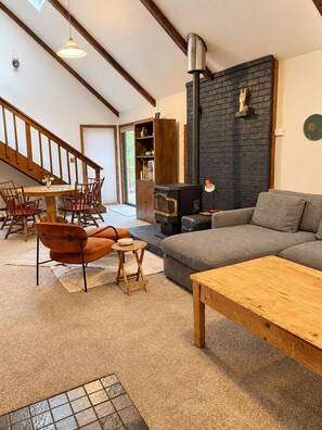 Un salón amplio con chimenea, un sofá, una mesa de comedor con sillas y una escalera.