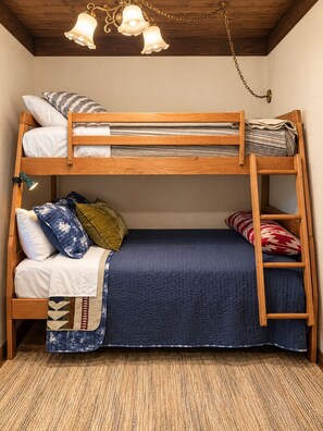 A bunk bed with a wooden frame, a blue quilted bedspread, and a decorative lamp above.