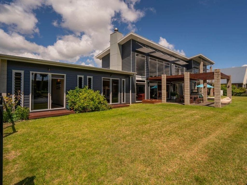 Une maison moderne à deux étages, dotée d’une grande pelouse, d’un patio couvert et d’un garage.