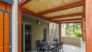 An outdoor patio with a wooden ceiling, a table with chairs, and a view of greenery.