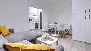 A modern living room with a grey sofa, a small white table with a decorative item, and a dining area with a white table and chairs.