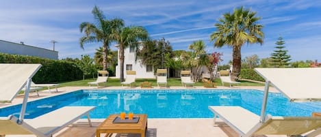 A swimming pool with lounge chairs and a table, surrounded by palm trees and a clear sky.