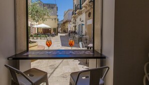 A view from a balcony with a table and chairs, overlooking a street with outdoor seating and buildings. - Pool - Private veranda and complete privacy - View of the private garden (San Vito Dei Normanni)