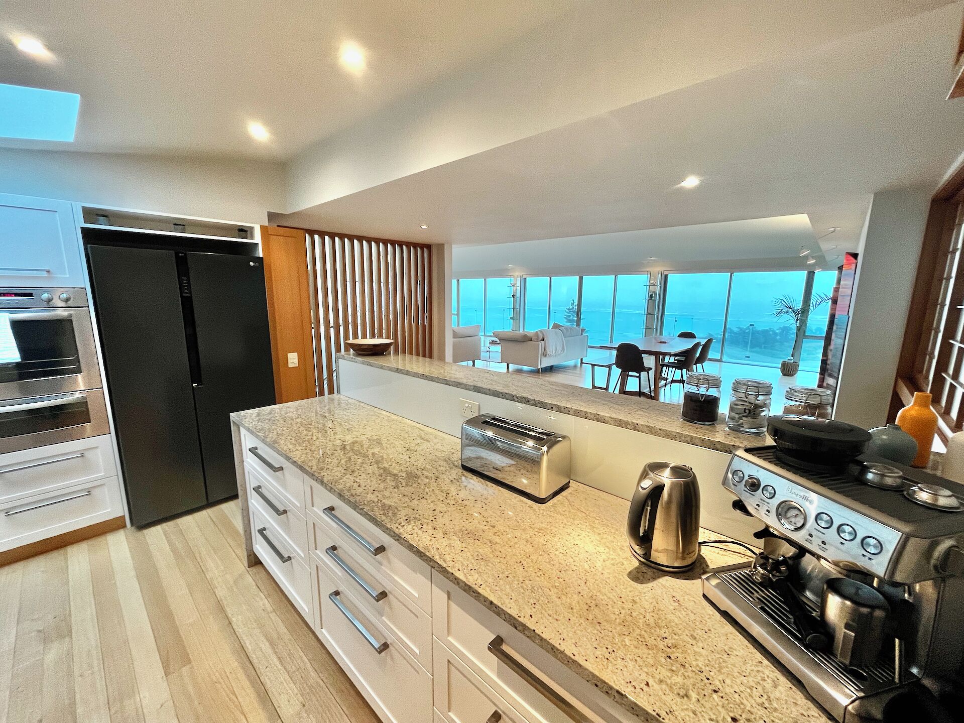 A modern kitchen with a large island, built-in oven, and espresso machine.