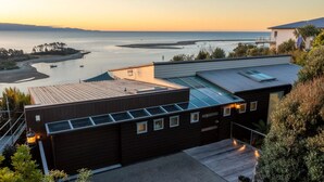 Un bâtiment moderne doté d’un toit plat, de grandes fenêtres et offrant une vue sur l’océan au coucher du soleil.