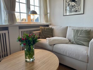 Un salon avec un canapé beige, une table ronde en bois et un vase de tulipes rouges.