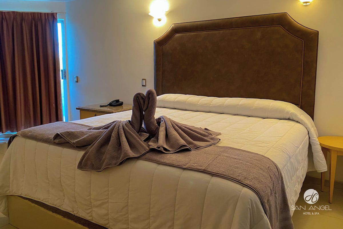 Une chambre d’hôtel avec un grand lit, une table de chevet avec un téléphone et un luminaire fixé au mur.