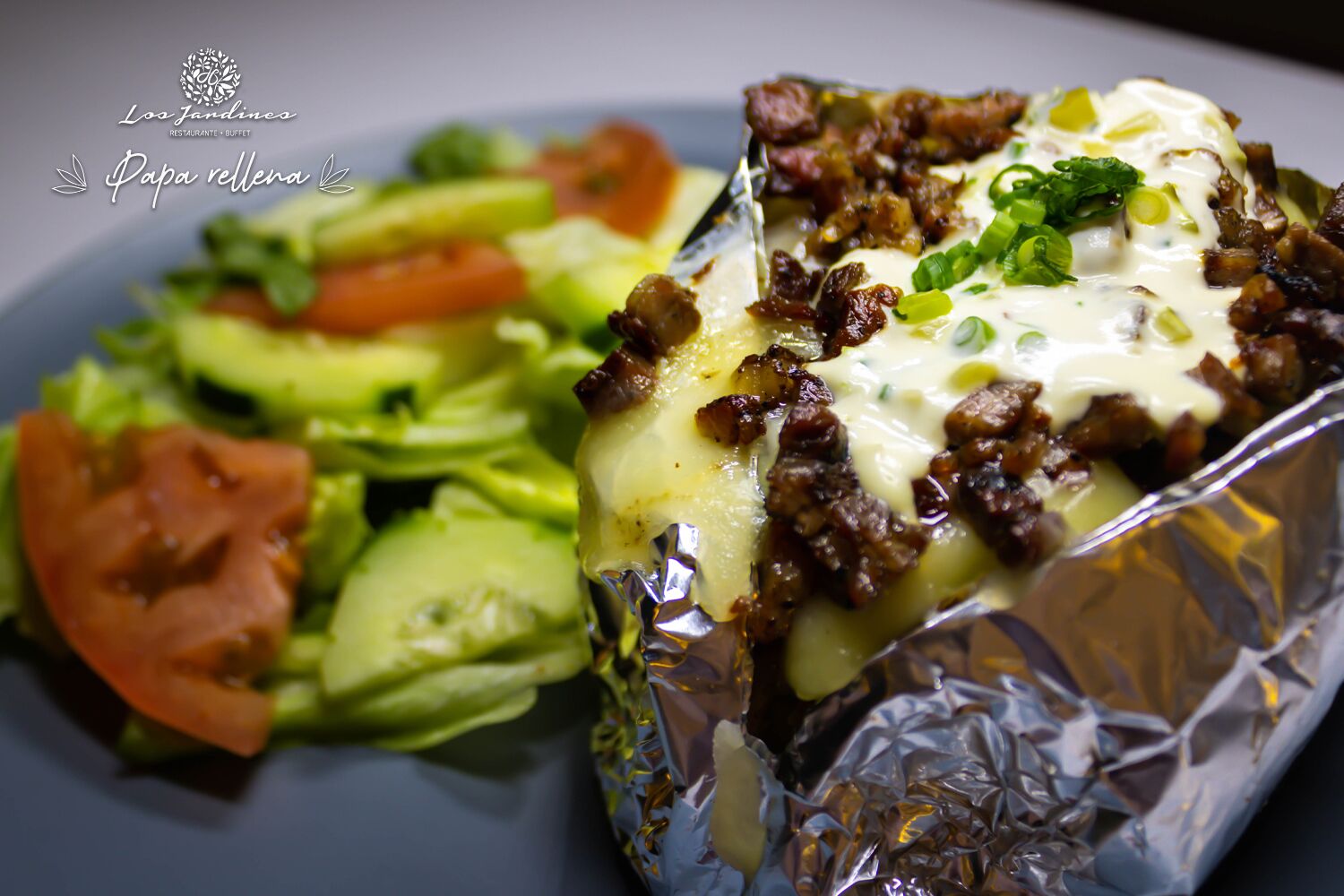 Un plato envuelto en papel de aluminio con queso derretido y carne, acompañado de una ensalada con lechuga, tomates y pepinos.