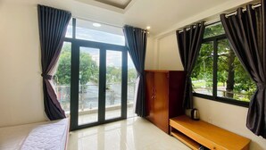 Una habitación con una cama, un banco de madera, una mesita y vistas a la calle y al verdor exterior.
