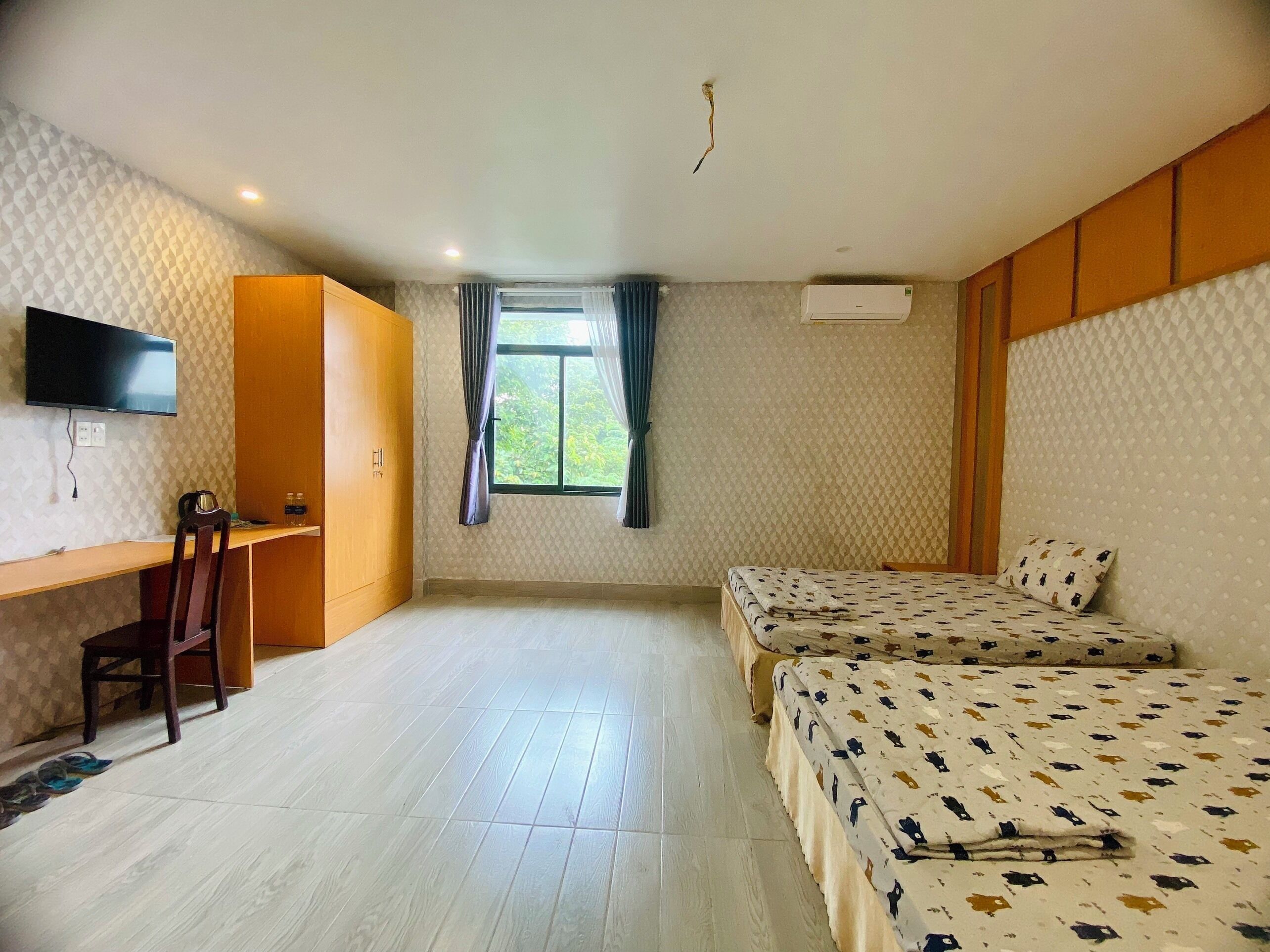 A hotel room with a bed, a desk, a chair, a TV, and a window with curtains.