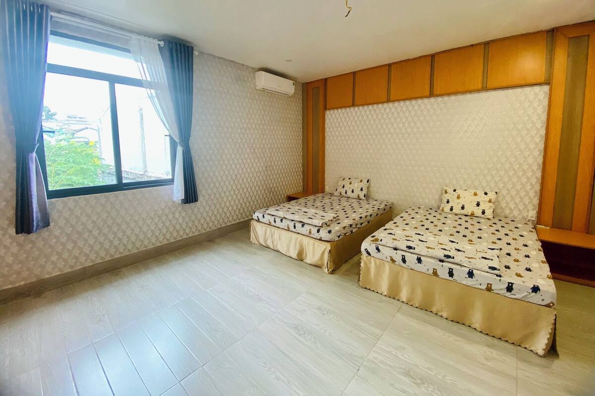A room with two beds, a window with curtains, an air conditioning unit, and a patterned wall.