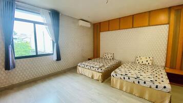 A room with two beds, a window with curtains, an air conditioning unit, and a patterned wall.