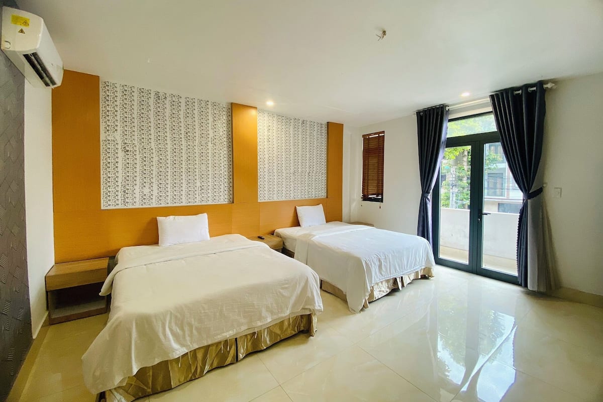 A hotel room with two beds, a large window with curtains, a wall-mounted air conditioner, and a patterned wallpaper.