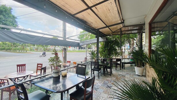 Un café al aire libre con mesas y sillas, plantas en macetas y vista a la calle.