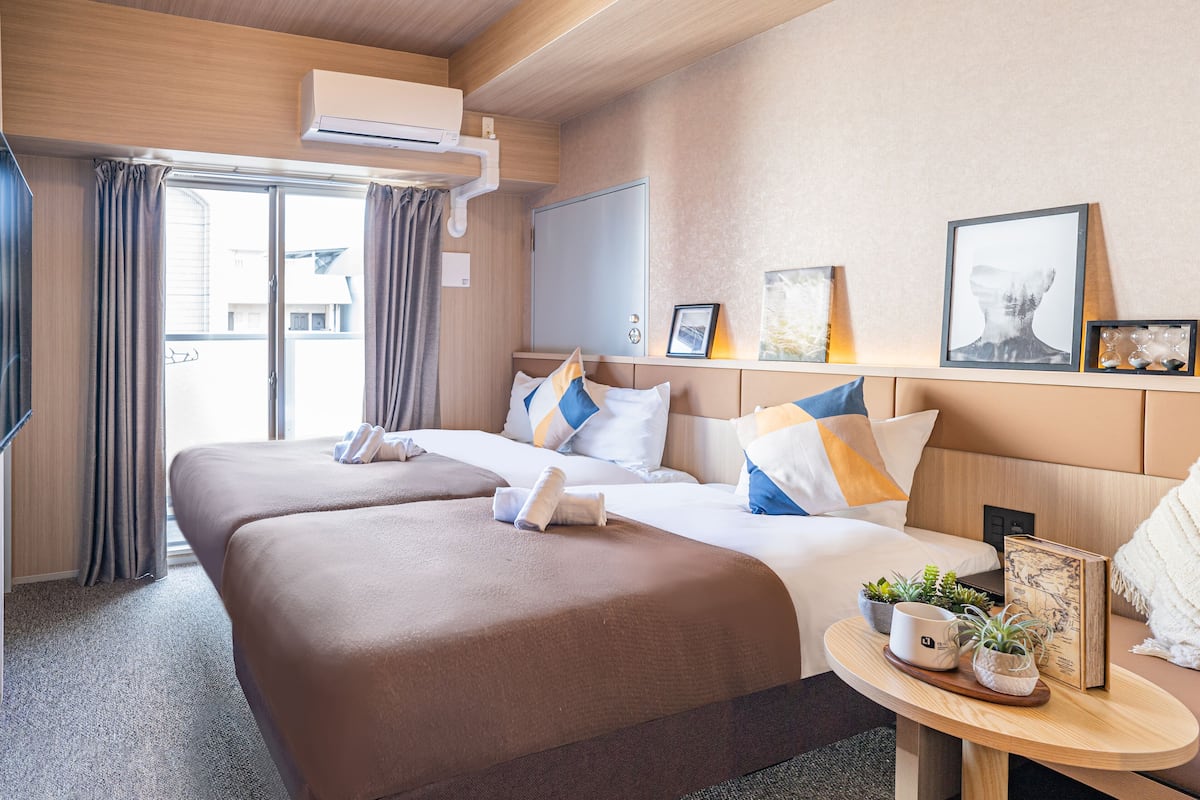 A hotel room with two beds, a small table with a map and a mug, and a window with curtains.
