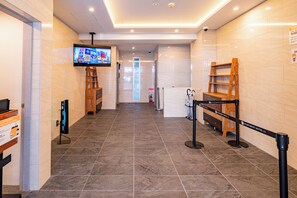 A hotel lobby with a tiled floor, a television mounted on the wall, a wooden bench, and a security barrier. - Apartment Hotel 11 Namba Minami (Osaka)