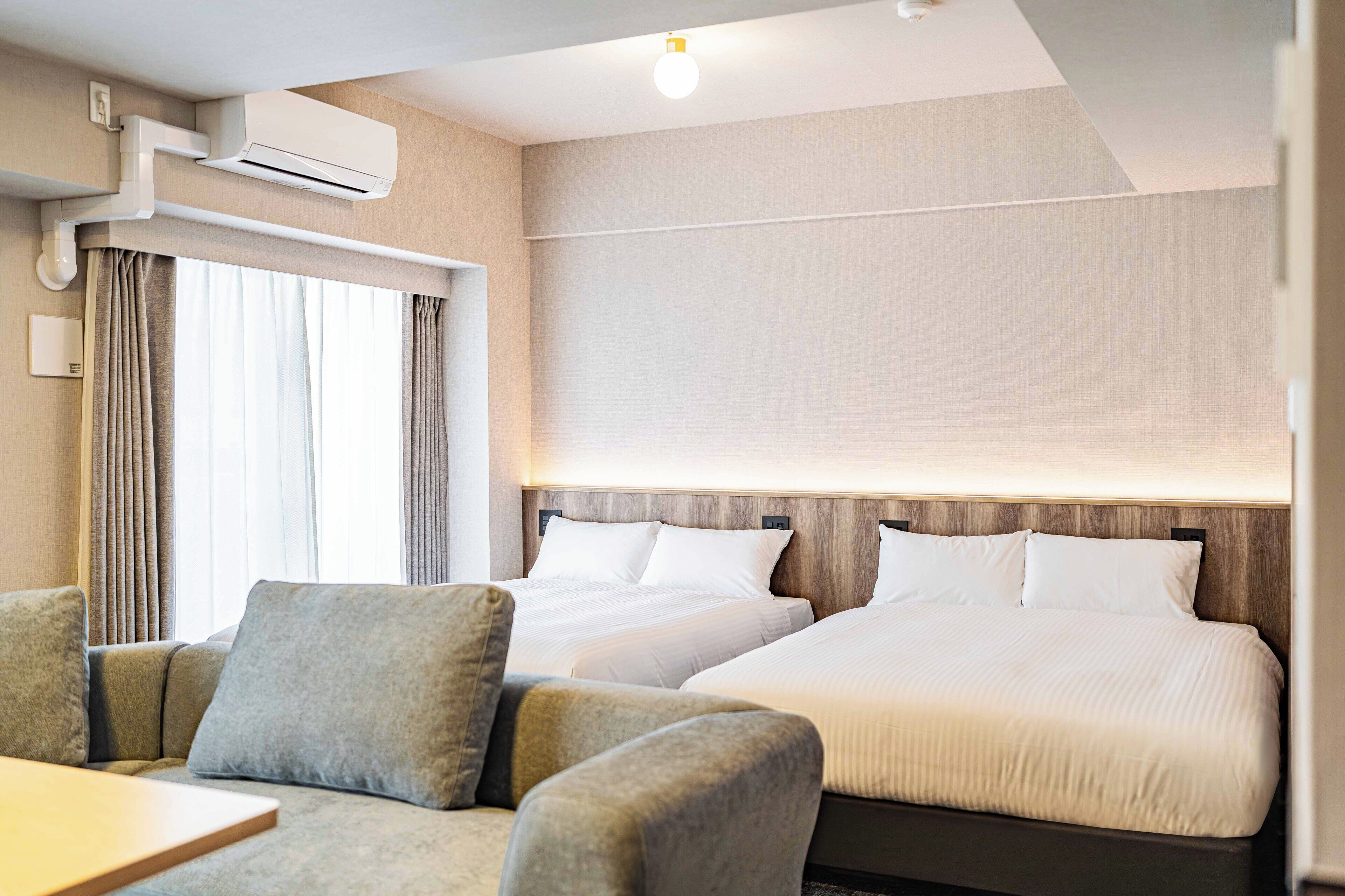 Una habitación de hotel con dos camas, un sofá y un aire acondicionado.