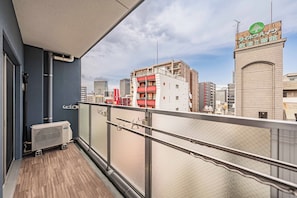 Un balcon donnant sur un paysage urbain, avec notamment un bâtiment arborant un logo vert.