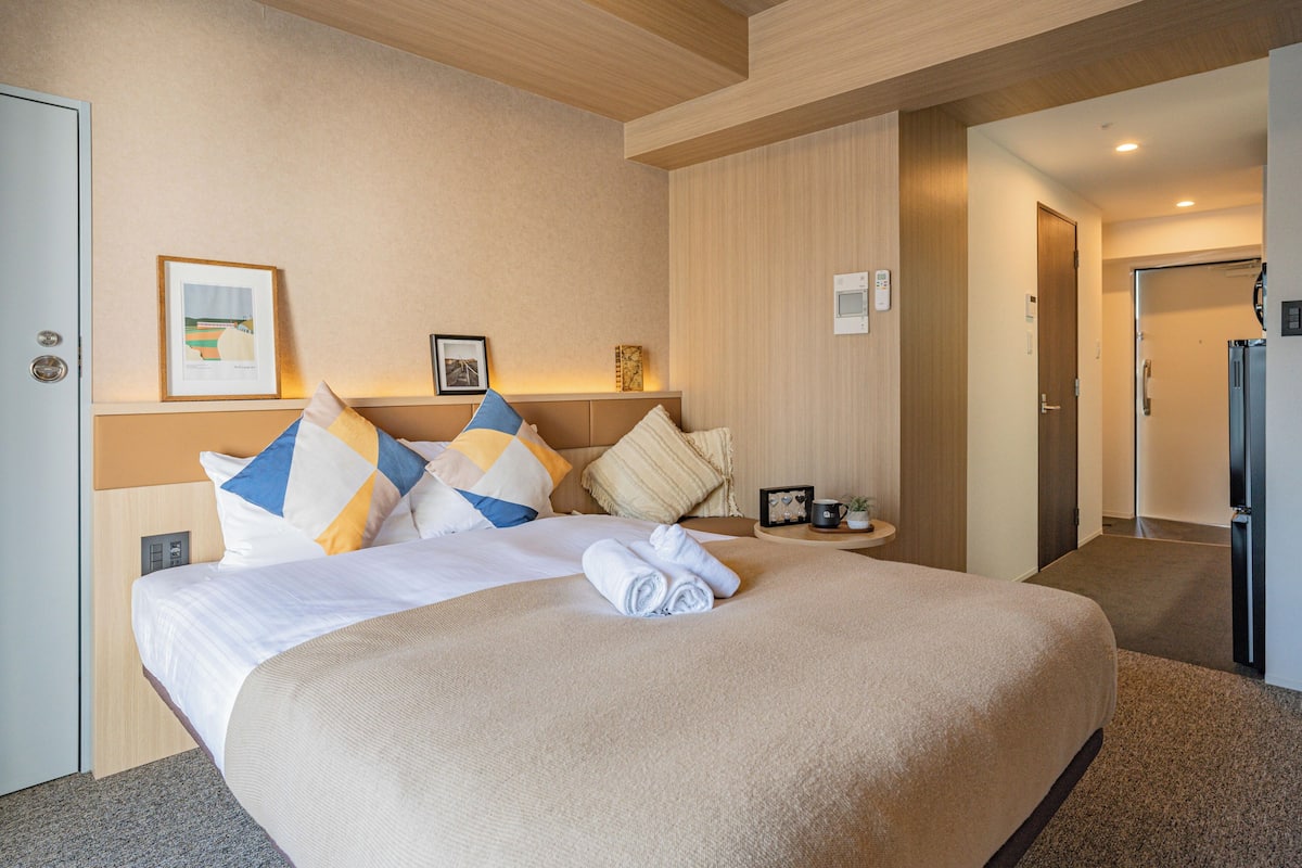 A hotel room with a large bed, a bedside table, a framed picture, and a refrigerator.