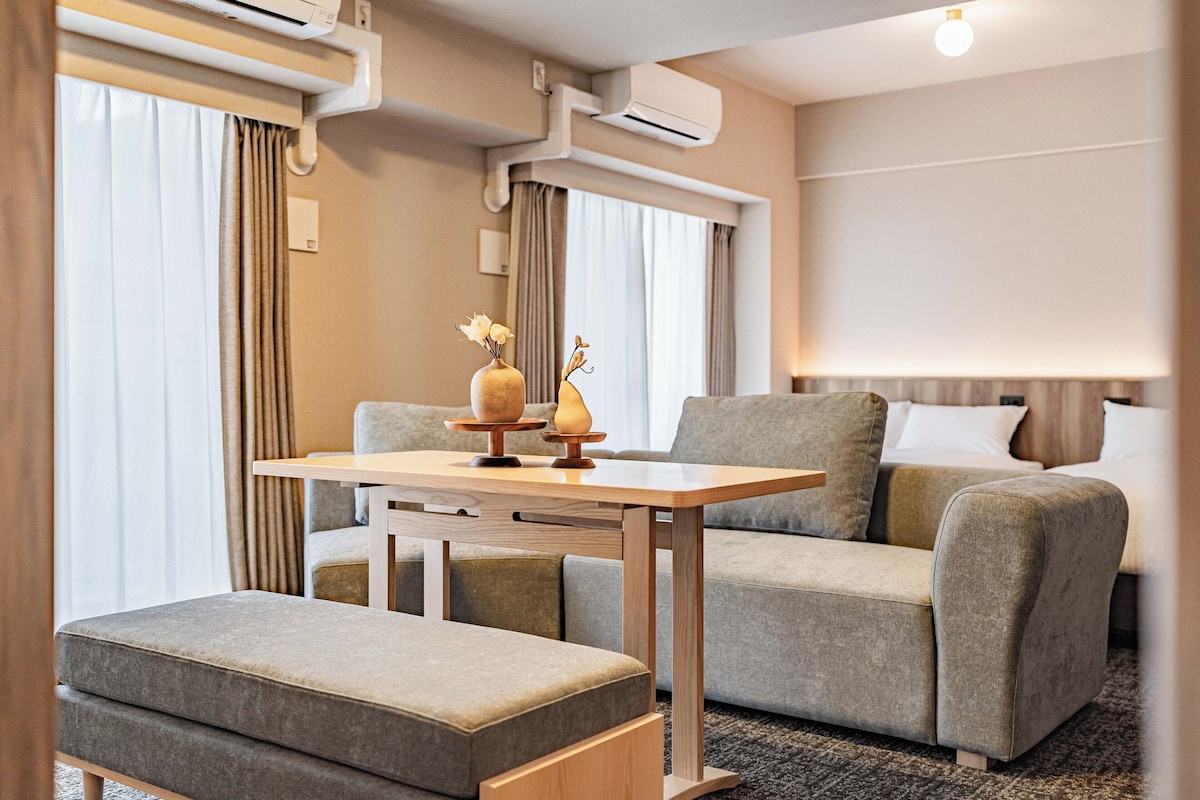Una habitación de hotel moderna con sofá, otoman y una mesita con adornos.