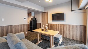 Un espacio habitable compacto con sofá, una mesita, una zona de cocina y un televisor de pared.