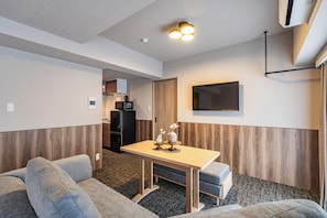 A compact living space with a sofa, a small table, a kitchen area, and a mounted TV. - Apartment Hotel 11 Namba Minami (Osaka)