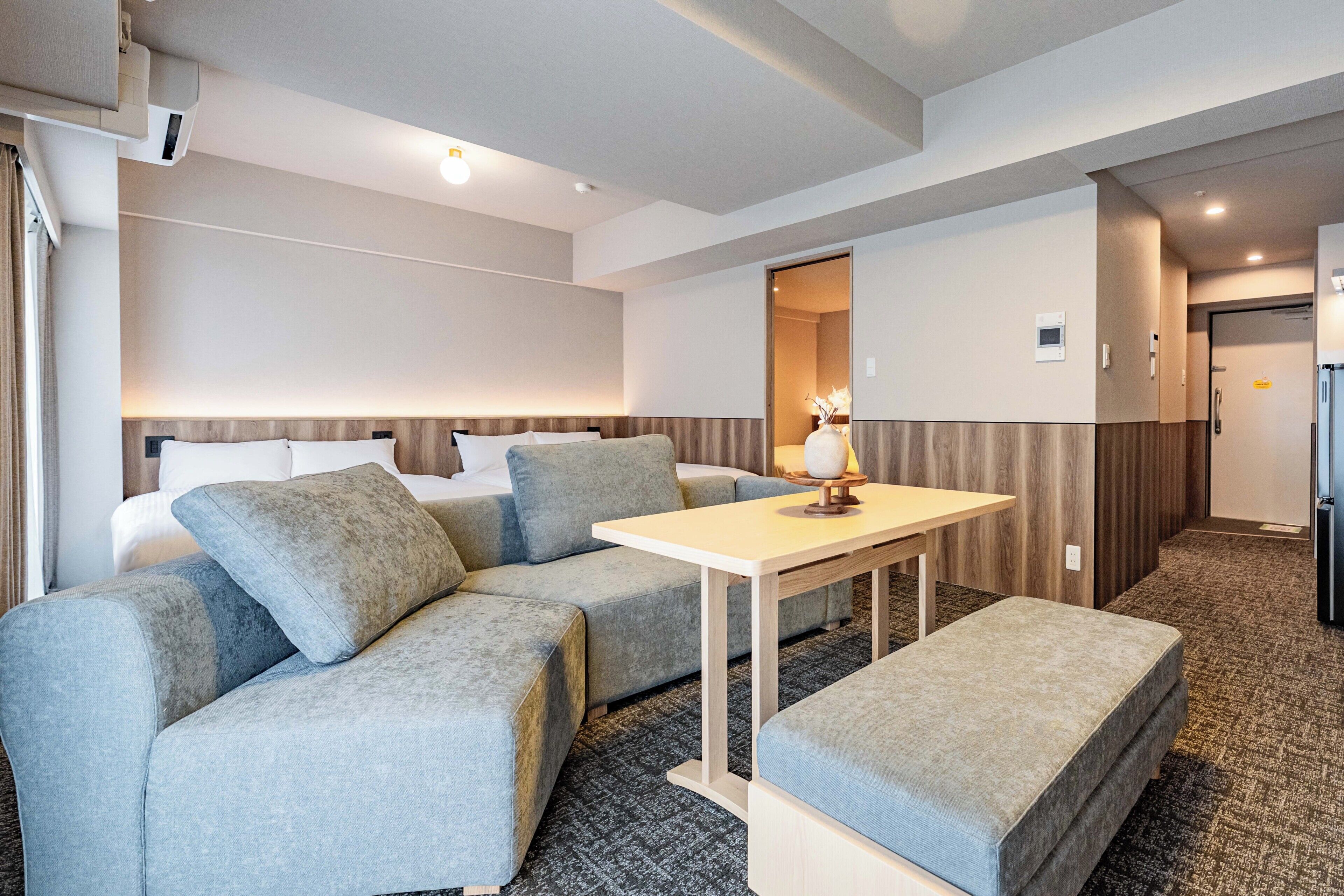 A hotel room with a bed, a sofa, a small table, and a kitchenette area.