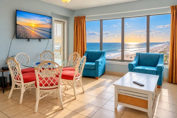 A room with a beach view, a television, wicker chairs with red cushions, a blue sofa, and a white coffee table.