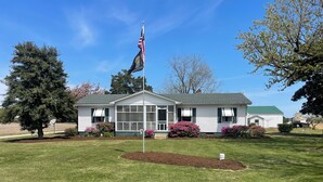 Ein zweistöckiges Haus mit Veranda, Fahnenmast mit US-amerikanischer Flagge und einem gepflegten Rasen.