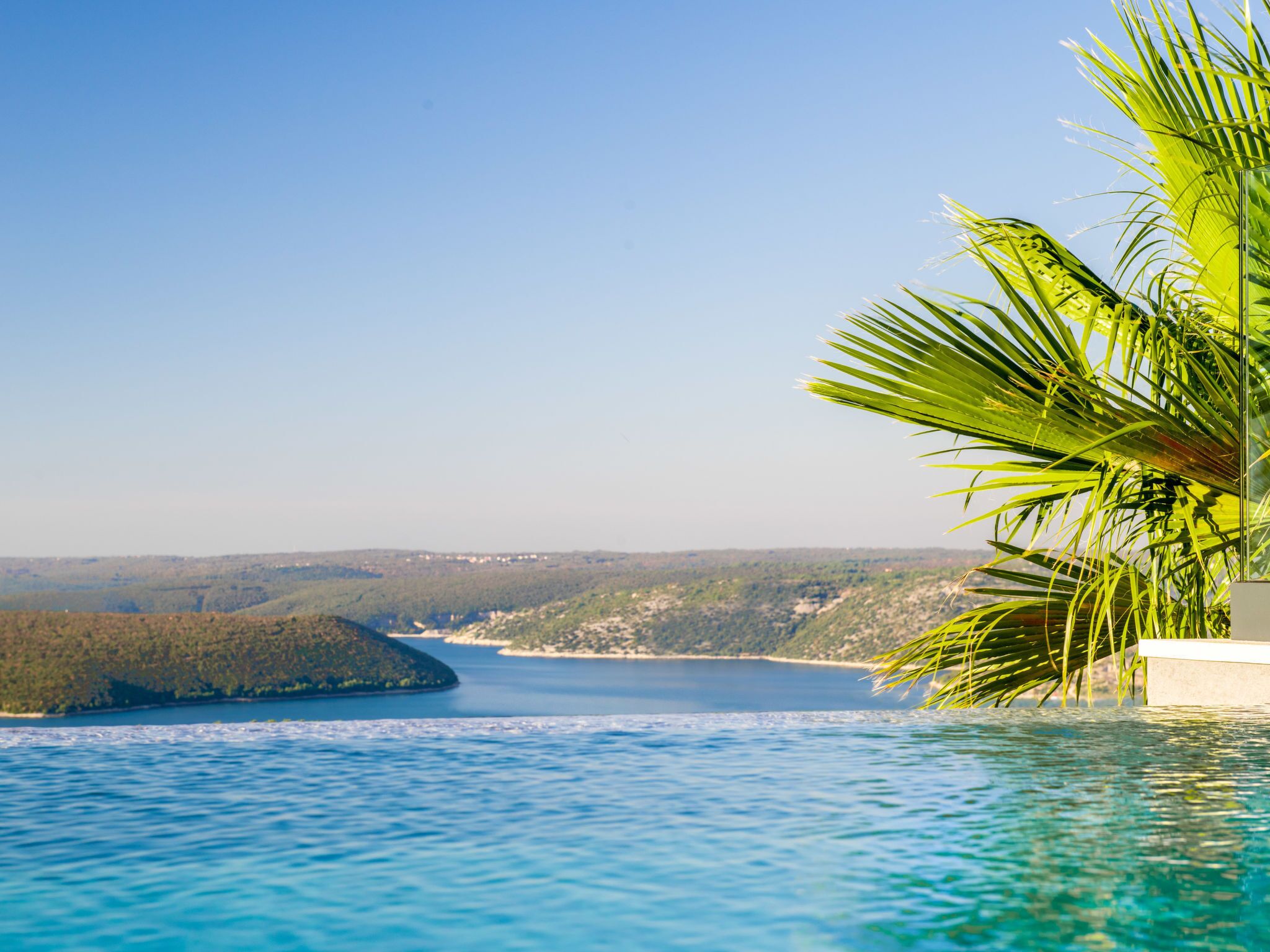 Vista despejada de una piscina con una palmera a la derecha y una vista distante de un lago y colinas.