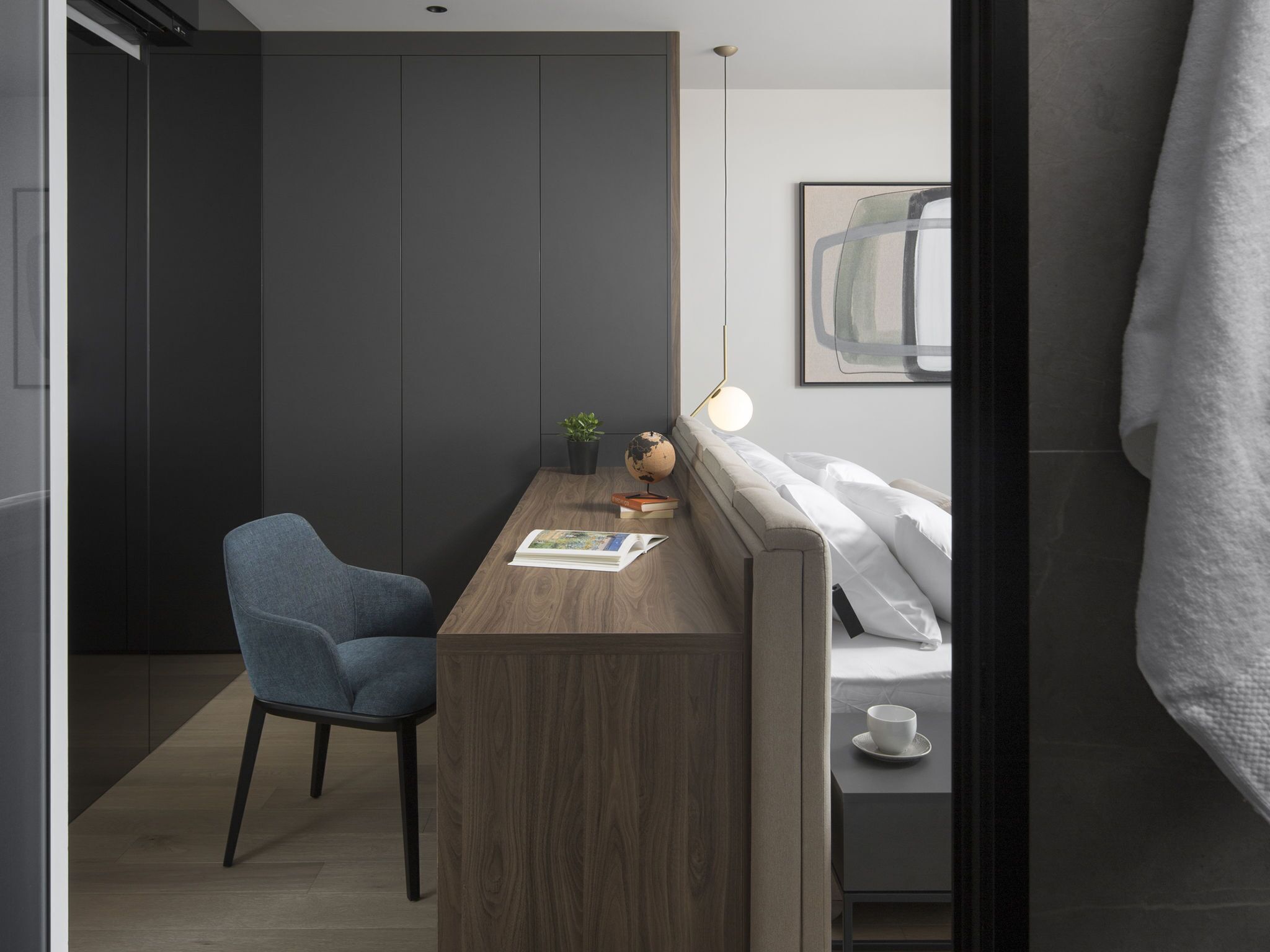 Een moderne, compacte slaapkamer met een houten bureau, een blauwe stoel, een wereldbol en een kleine plant.