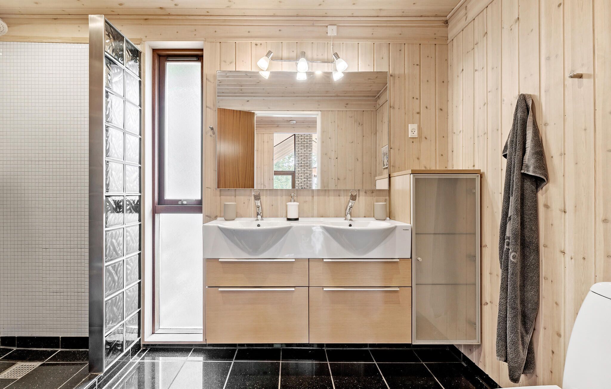 A modern bathroom with wooden paneling, a double sink vanity, and a towel hanging on the wall.