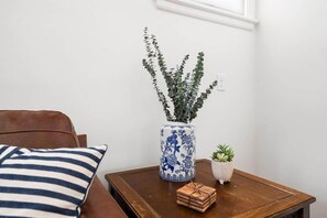 A room with a brown leather sofa, a striped pillow, a blue and white vase with a plant, a small potted plant, and a stack of folded towels on a wooden table.