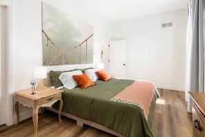 A bedroom with a bed, a nightstand, a lamp, and a large wall painting. - Square Haven Duplex -Walk to Pubs Cafe & Ice Cream (Washington)