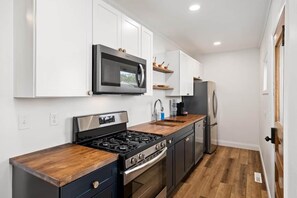 A modern kitchen with white cabinetry, a stainless steel stove, a microwave, and a refrigerator. - Square Haven Duplex -Walk to Pubs Cafe & Ice Cream (Washington)