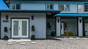 Une maison moderne à deux étages, avec une façade bleue, une porte d’entrée et deux plantes en pot.
