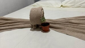 A neatly made bed with a grey headboard, a beige blanket, and a small potted plant on the bed. - La Casa De Detours Costa Rica (La Fortuna)