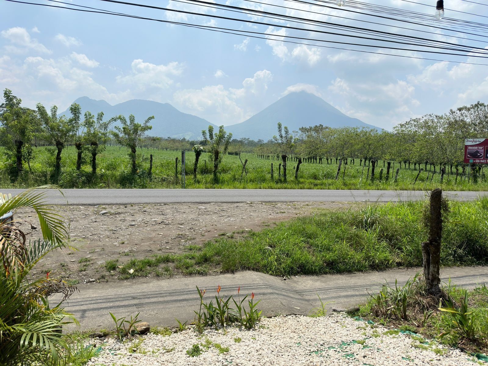 Paisaje rural con una carretera, campos verdes y una montaña al fondo.