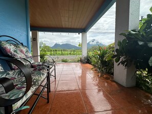 A covered patio with a bench and potted plants, overlooking a mountainous landscape. - La Casa De Detours Costa Rica (La Fortuna)