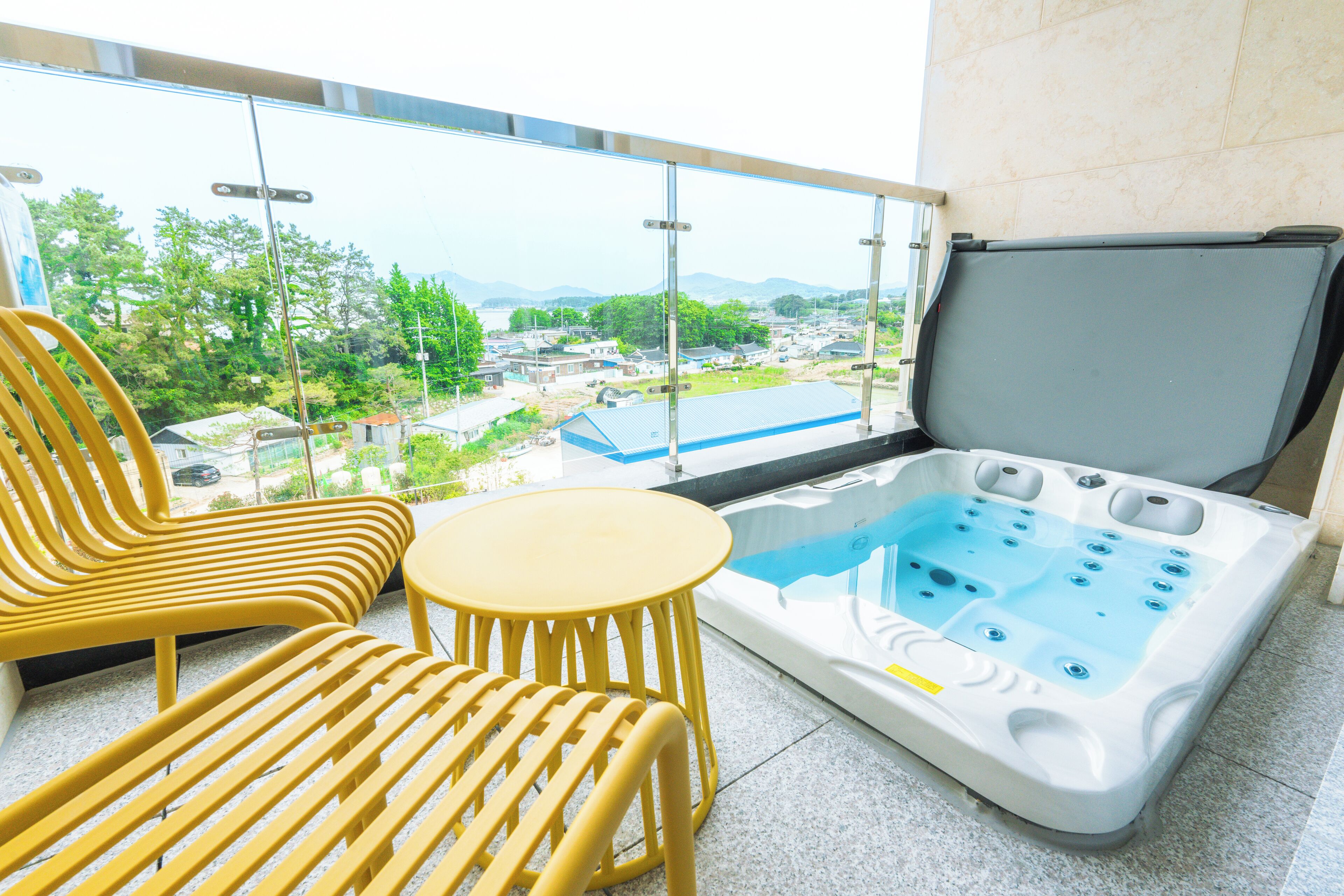 A balcony with a hot tub, two yellow chairs, and a small table.