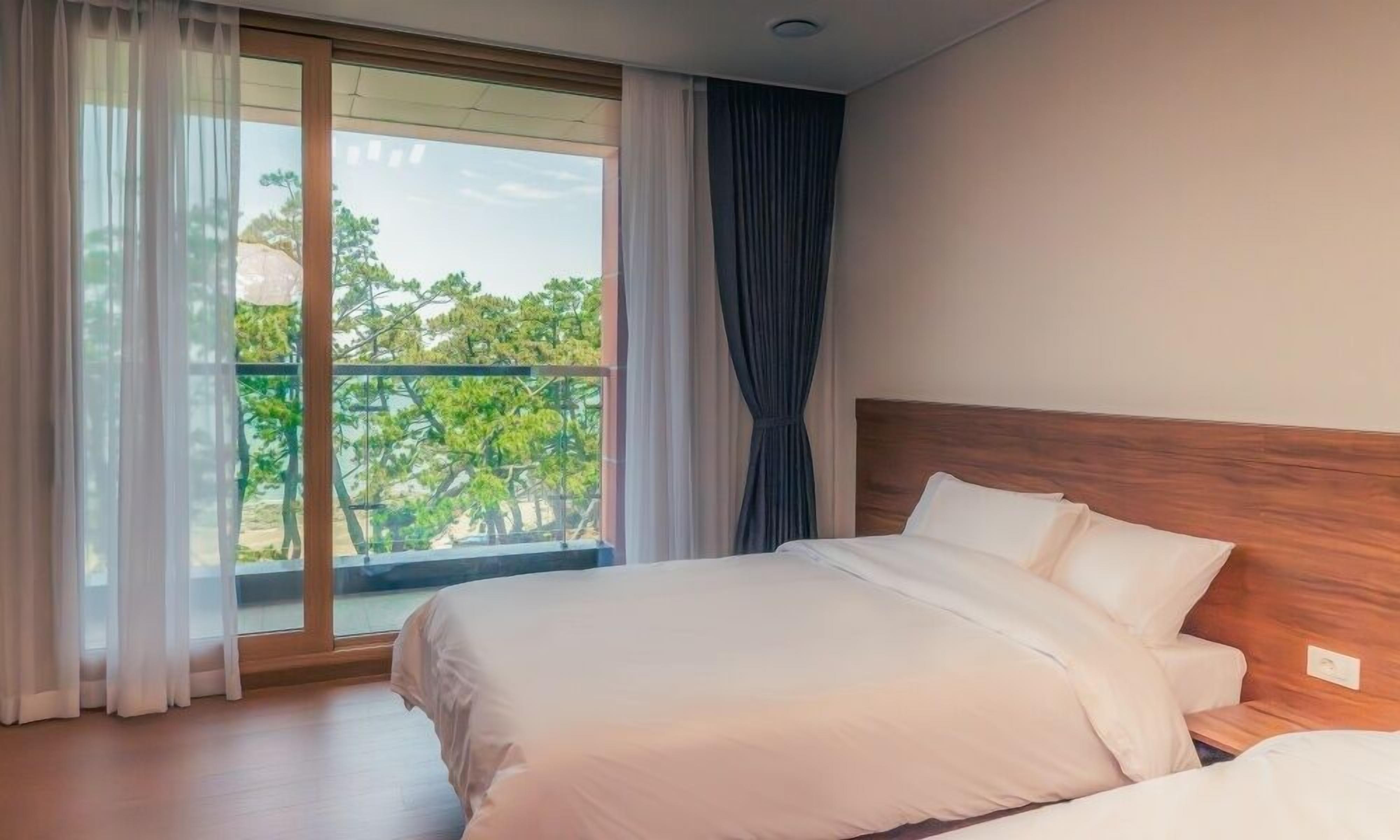 A hotel room with a large window, a wooden headboard, and a bed with white bedding.