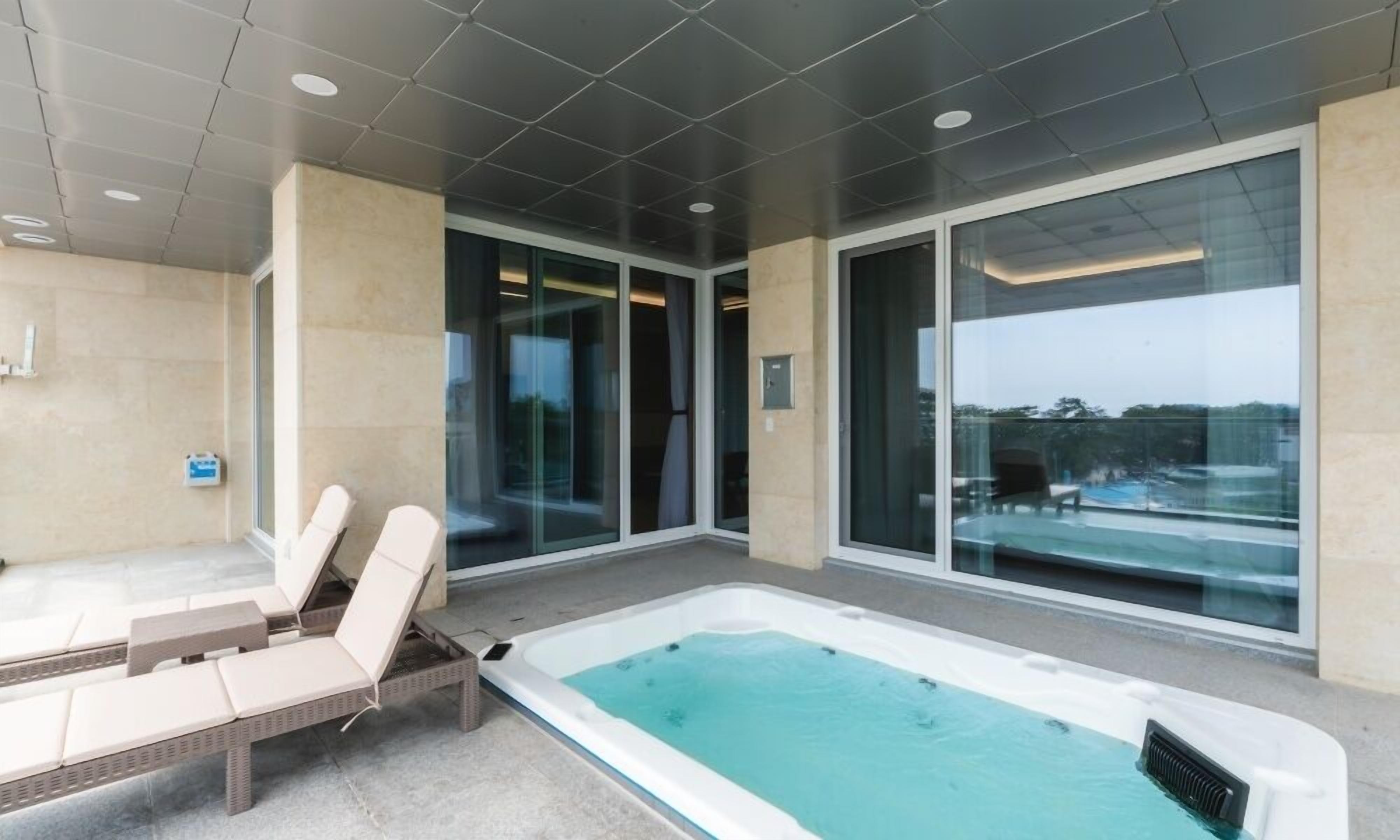 A modern indoor pool area with lounge chairs and a hot tub.