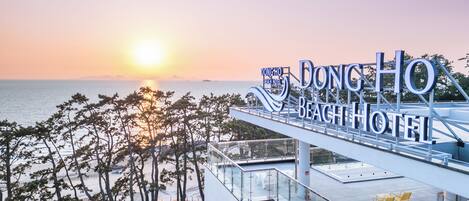 Un hotel moderno con terraza en la azotea con vistas al mar, que presenta un cartel llamativo del Hotel Dong Ho Beach.