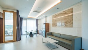 A modern living room with a sofa, a coffee table, and a dining area with chairs. - DONGHO BEACH HOTEL (Gochang)