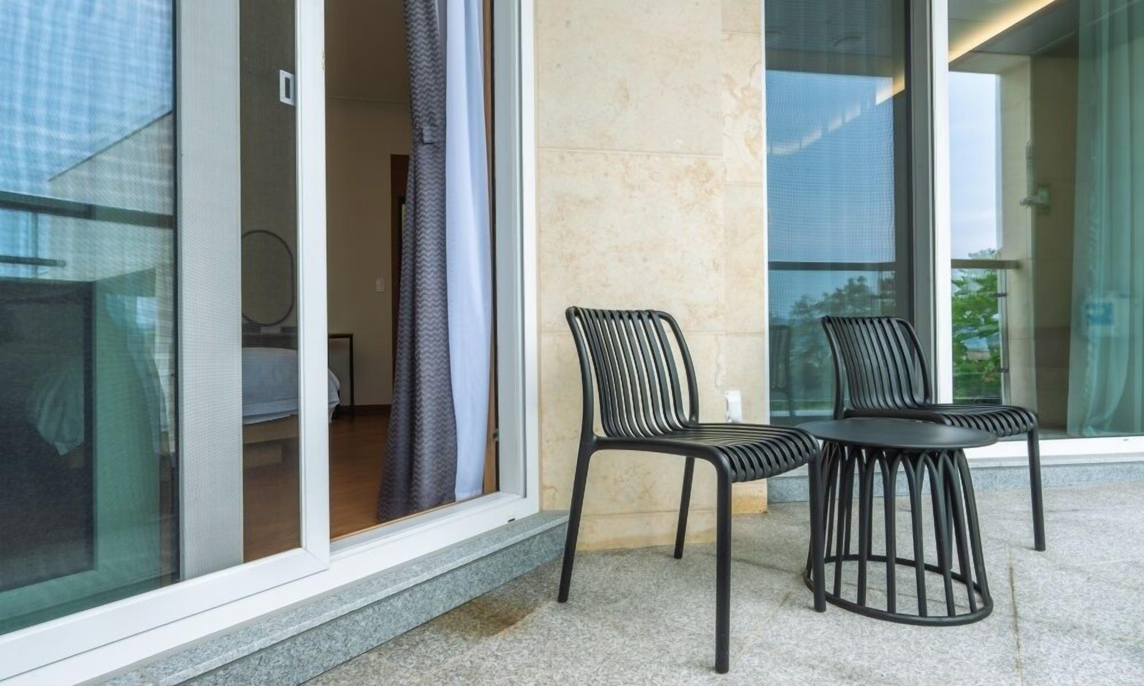 Ein modernes Hotelzimmer mit Balkon, ausgestattet mit zwei schwarzen Metallstühlen und einem kleinen Tisch.