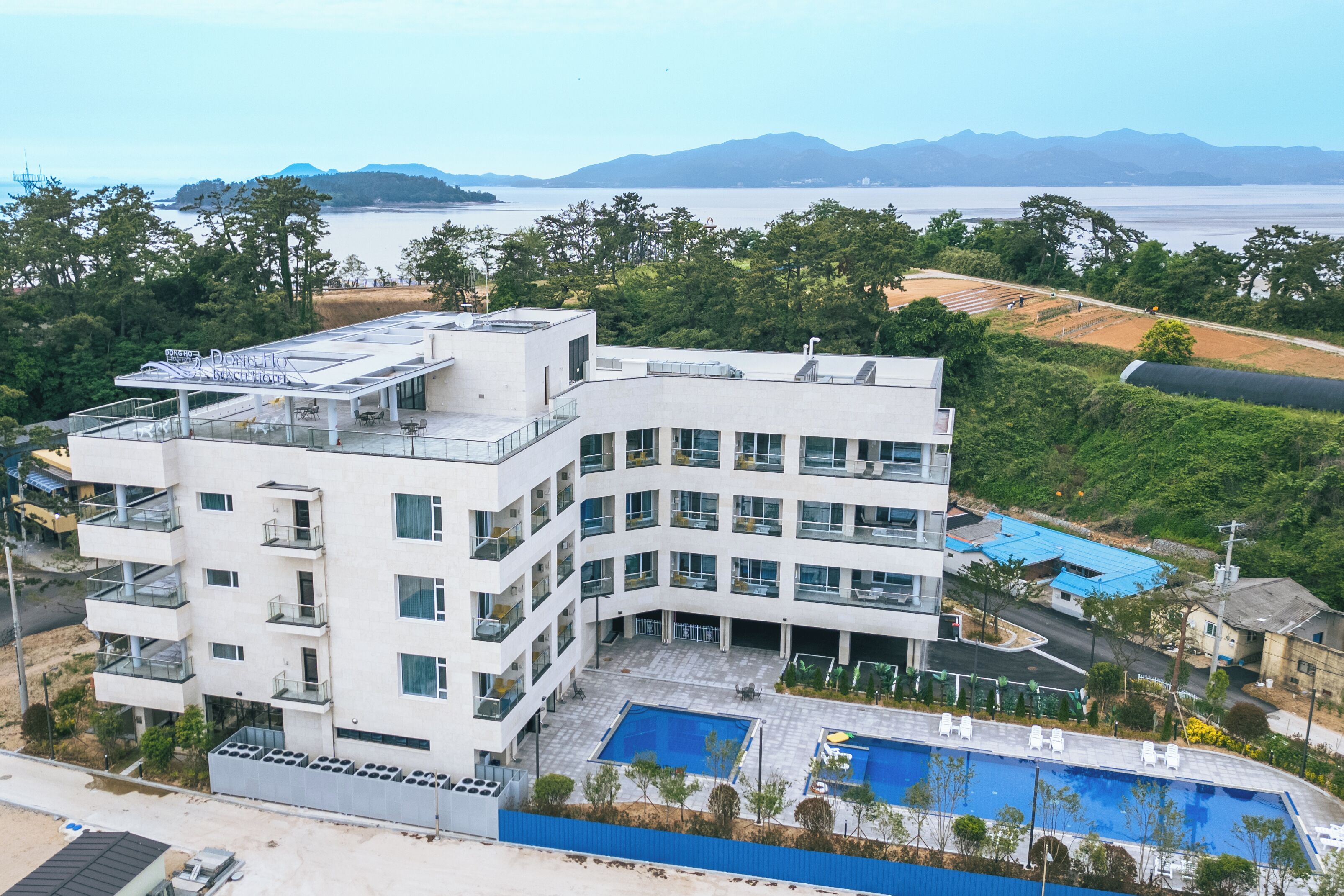 A modern multi-story hotel with a rooftop pool and a view of the sea.